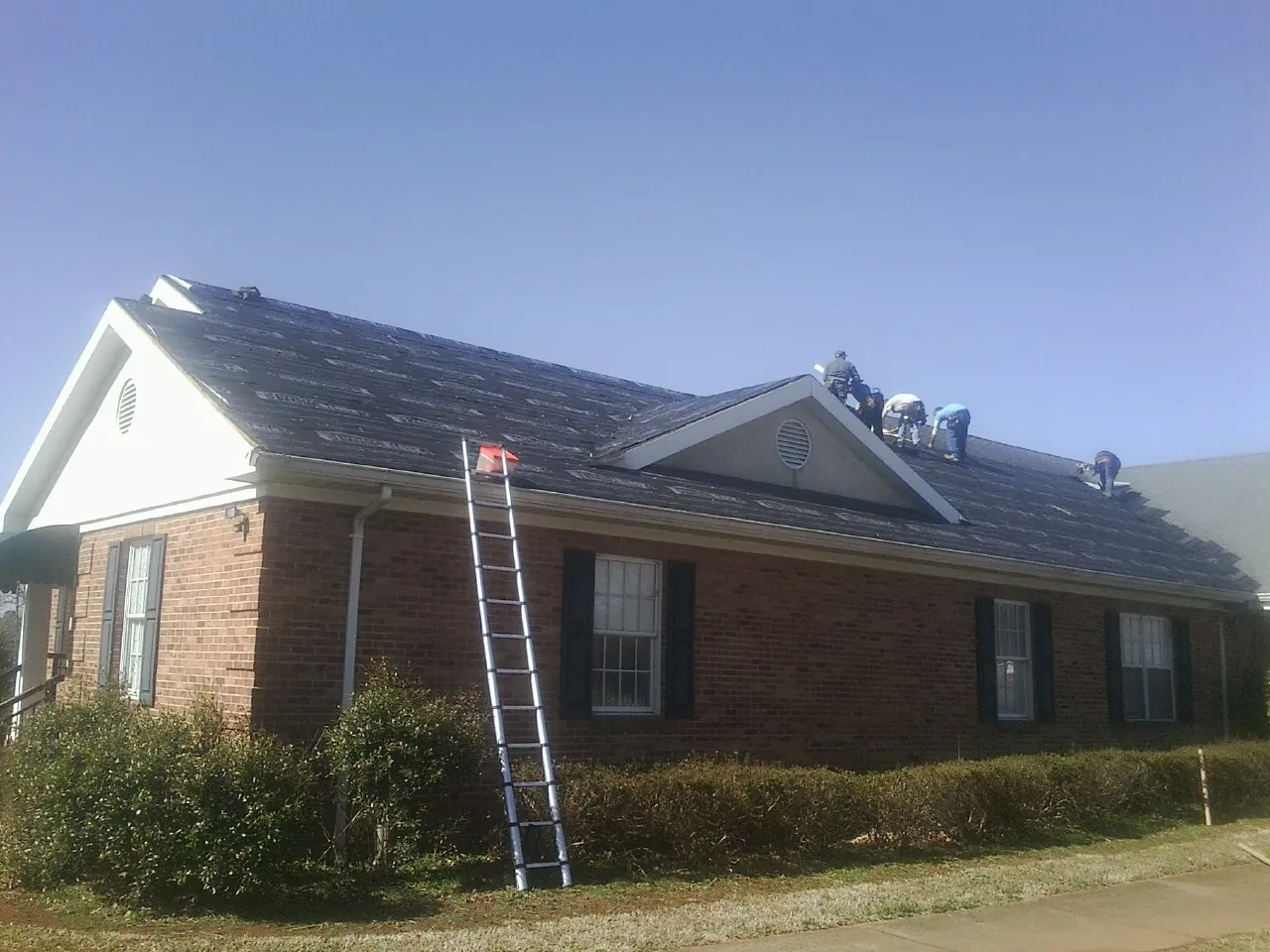 Crew tearing shingles off a brick ranch roof with a ladder set — Emergency Roof Repair work by our crew in Morrow