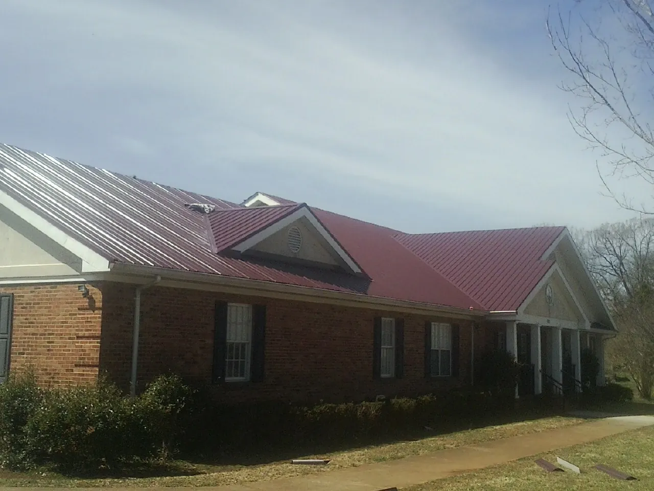 Red metal roof with gabled entries on a long brick building, from a Hail Damage Roof Repair job in Morrow
