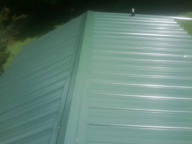 New green metal panels meeting at the ridge of a roof — Flat Roof Repair work by our crew in Morrow