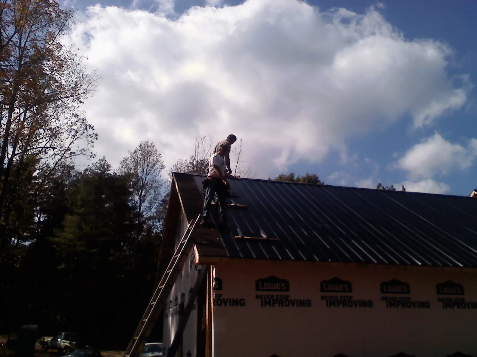 Roofer fastening dark metal panels high against a cloudy sky, from a Roof Inspection job in Morrow
