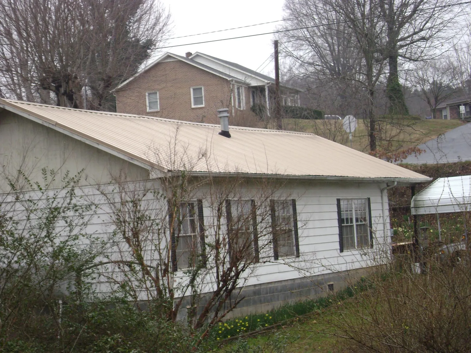 Tan metal roof on a white sided house set into a hillside — Commercial Roofing by Roofing Brothers in Morrow