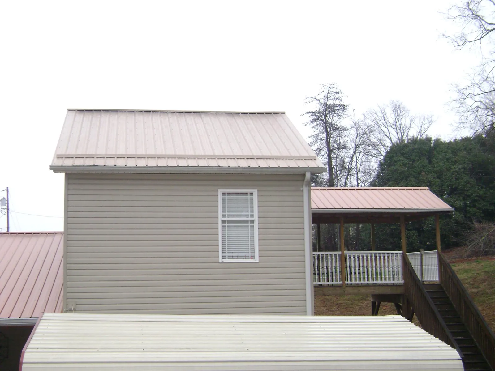 Tan metal roofs on a two story addition and attached porch, from a Roof Replacement job in Morrow